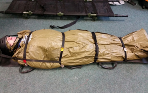figurant zabalený v termo izolačním vaku pro kontrolu hypotermie - HPMK (Hypotermia Prevention Management kit) a připravený k transportu na nosítkách SKED